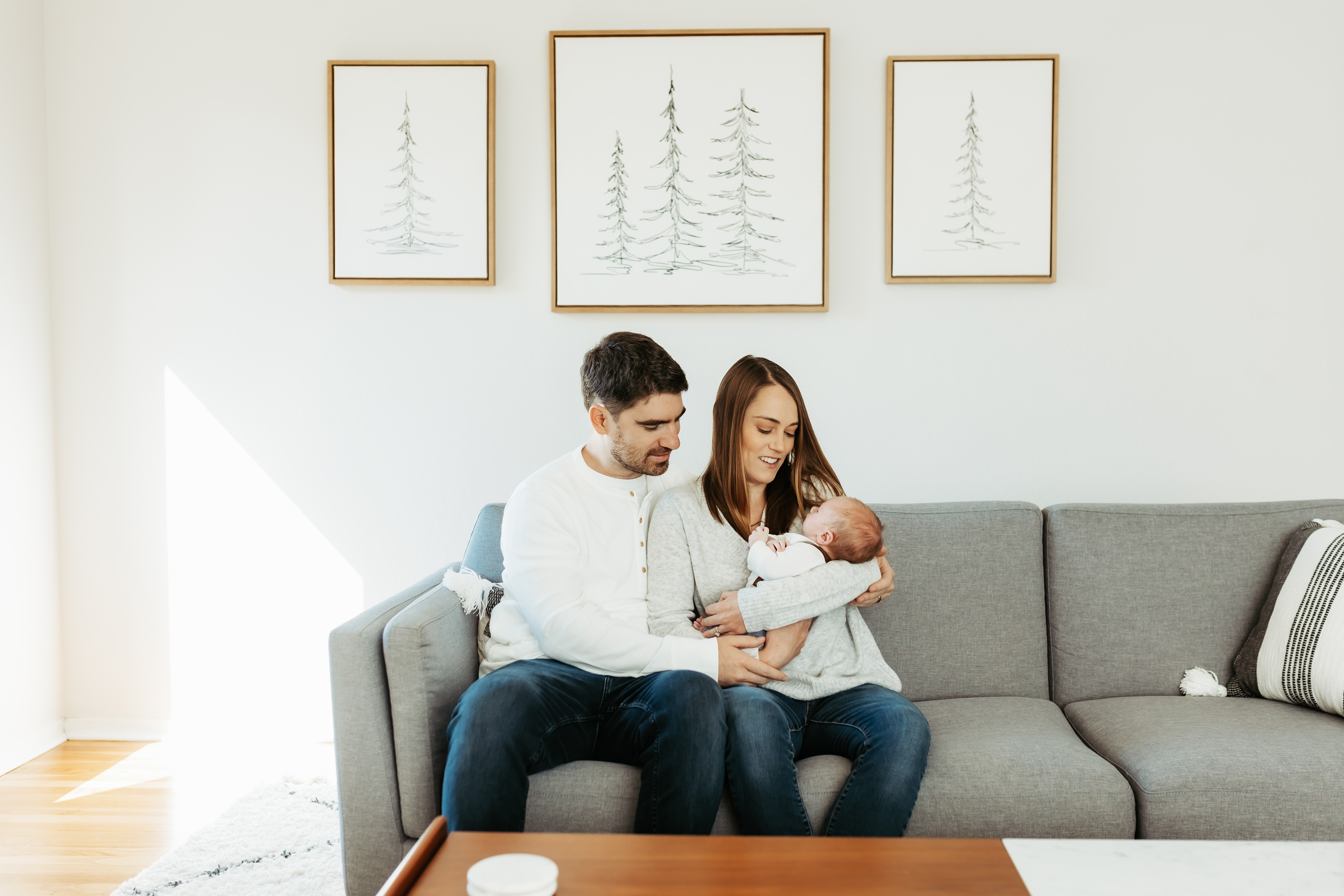 A mother and father sitting on the couch holding their newborn.