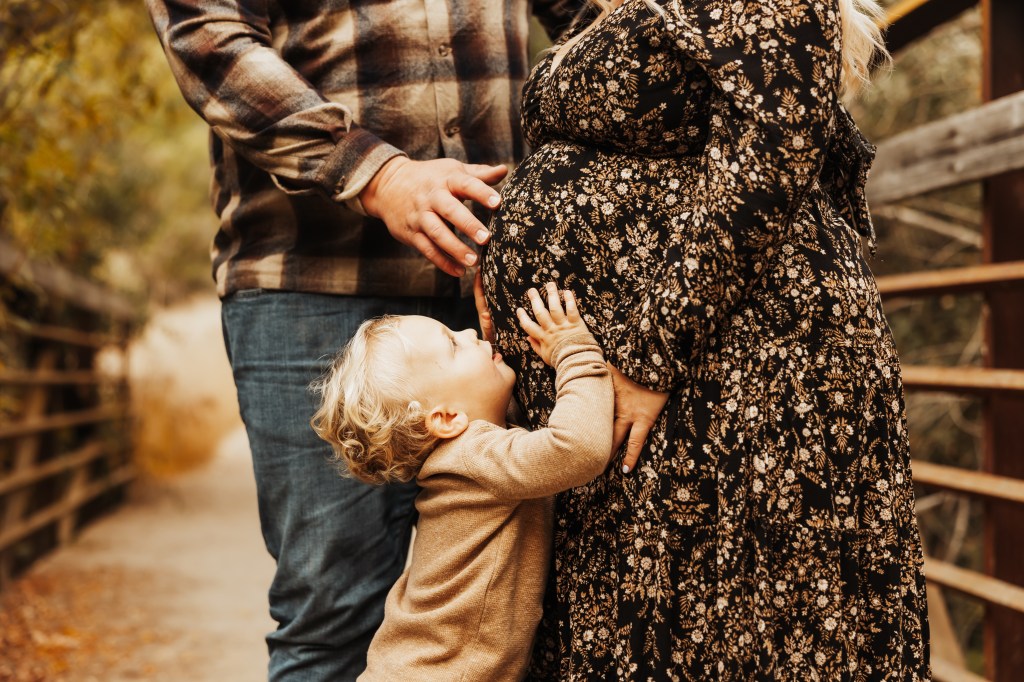 cropped images of toddler son kissing mother's pregnant belly and father's hand on mother's belly