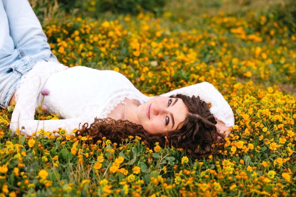 A graduating senior girl lays in a patch of wildflowers.