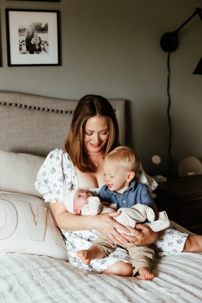 A mom hold a newborn baby and toddler in her lap doing an in home newborn photo shoot.