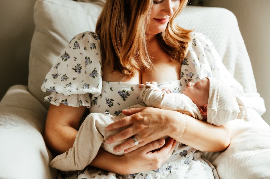 Mother hold sleeping newborn baby while sitting in an armchair.