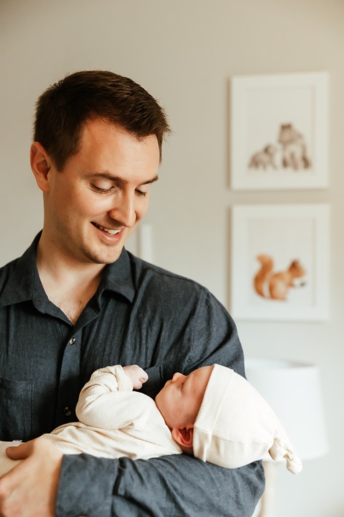A father holds his newborn son in the nursery during a newborn photo session.