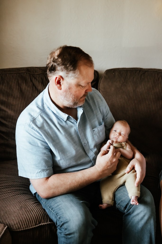 Dad holds his newborn son in his lap for a photo shoot.