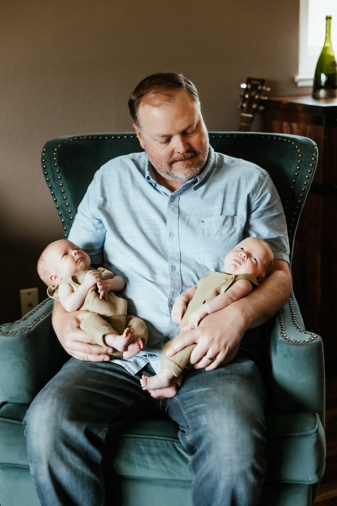 Father holds both his newborn babies in his lap.