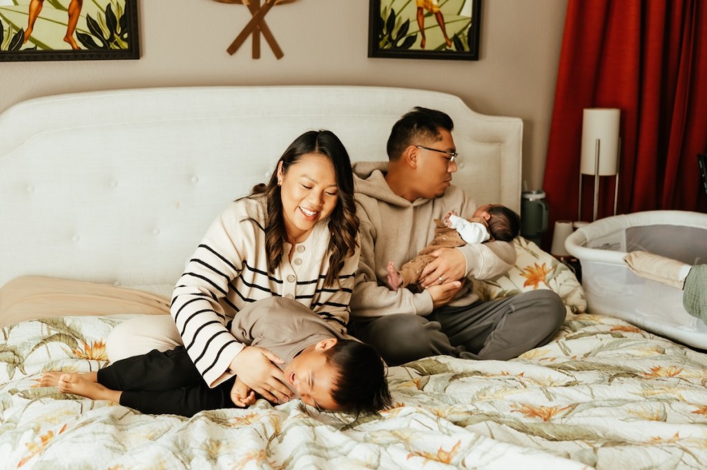 Parents playing with their young children at home on their bed.