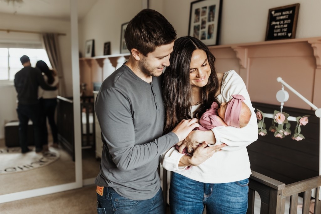 Mother and father cuddle newborn baby girl in the nursery.