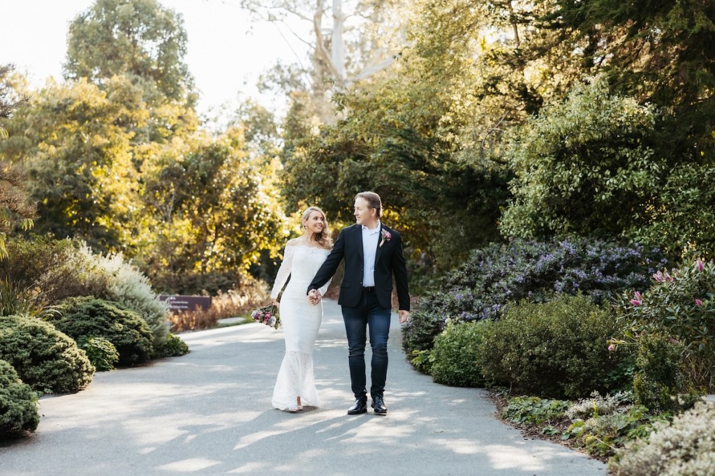 A bride and groom walk a path in the San Francisco Botanical Garden.