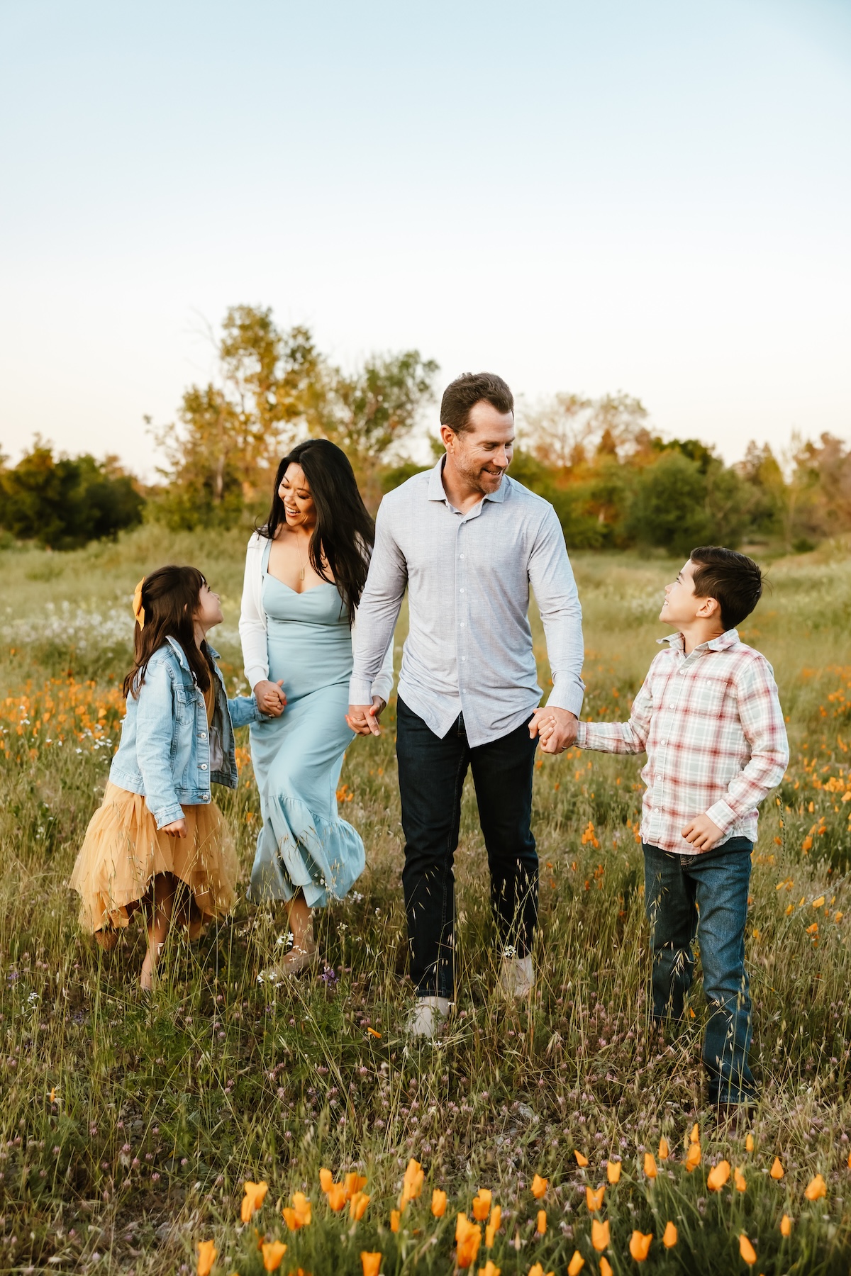  A family of four walk hand in hand through a wild flower field.