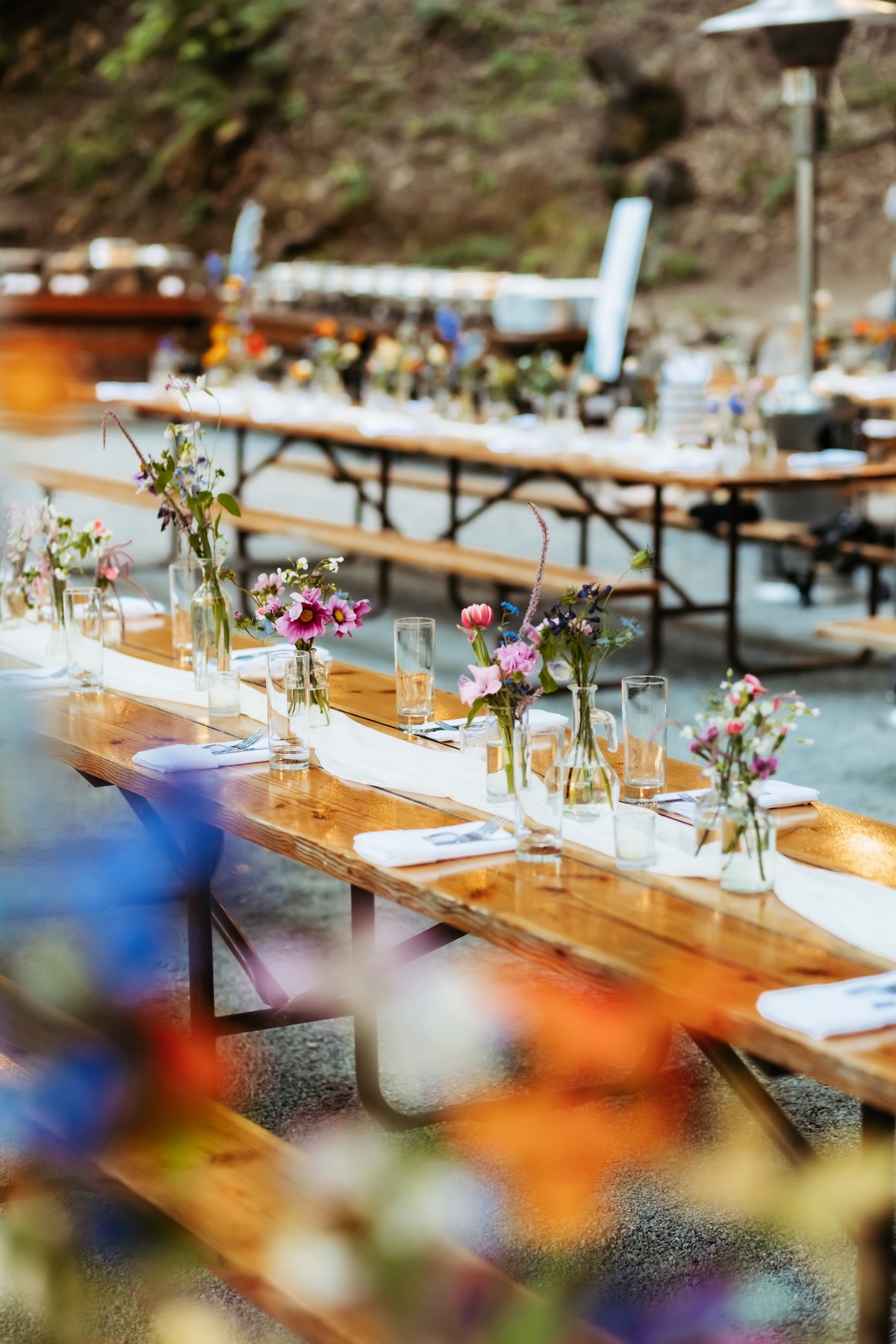 Table settings on wooden picnic tables with florals in bud vases by Zaddy Blooms in Redwood Grove, Saratoga Springs California.