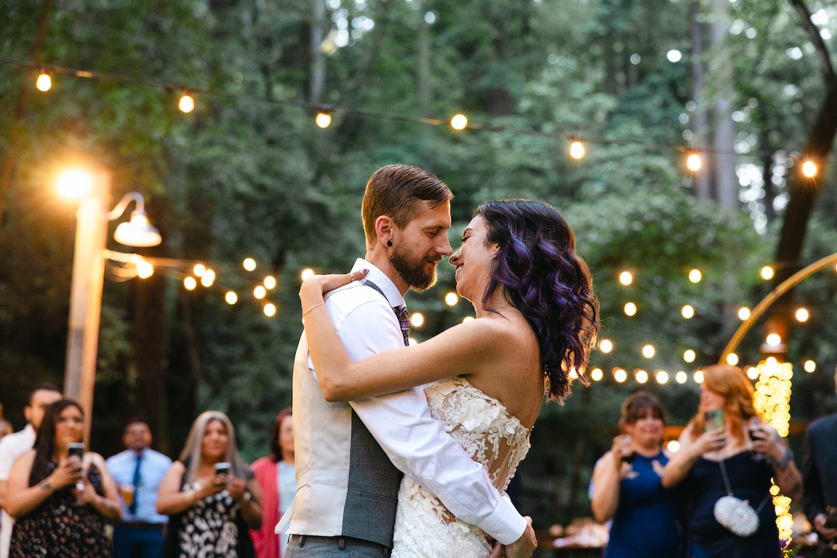 Couple's first dance as husband and wife under string lights at Cathedral Grove in Saratoga Springs California.