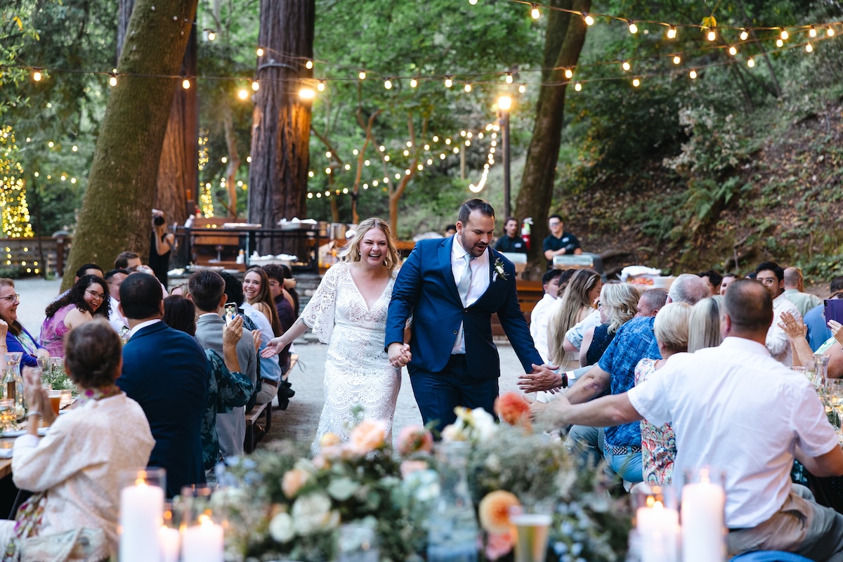 The Bride and Groom enter the party down the center of the picnic tables to the sweetheart table at Redwood Grove in Saratoga Springs California.